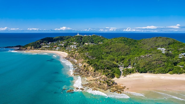 Une zone côtière comprenant une plage, un phare et une colline où se trouvent des bâtiments.