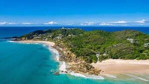 A coastal area with a beach, a lighthouse, and a hill with buildings.