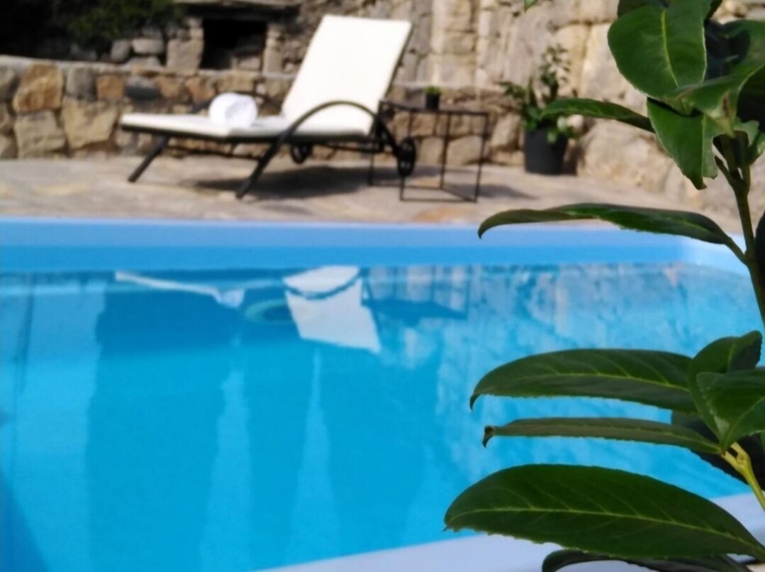 En swimmingpool med kristallklart blått vatten, en stenmur och en solstol i bakgrunden.