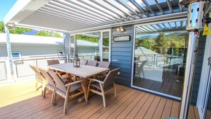A covered outdoor deck with a table and chairs, a sign reading "Great Alpine Road," and a view of the surrounding area. - VILLA URBANE : Bright (Bright)