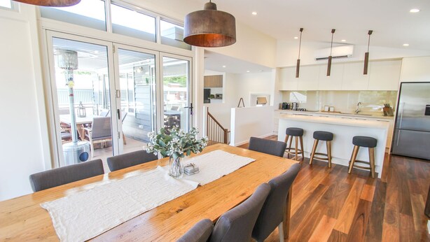 A modern kitchen with a central island, a dining area with a wooden table and chairs, and a large sliding glass door leading to an outdoor patio. - VILLA URBANE : Bright (Bright)