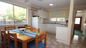 A compact kitchen with white cabinets, a refrigerator, and a dining area with a wooden table and chairs.