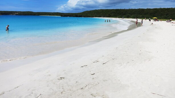 Una playa con agua cristalina, arena blanca y algunas personas.