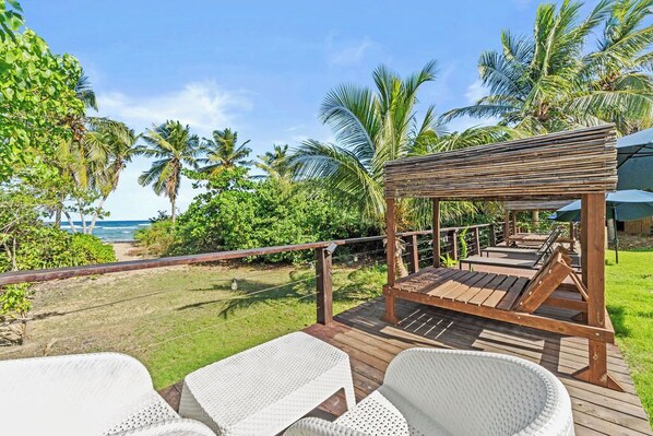 A wooden deck with white wicker chairs and a wooden pergola overlooking a beach. - Stunning Beach Front House,
beach door access 4BR (Vieques)