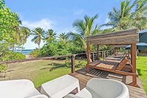Une terrasse en bois avec des chaises en osier blanc et une pergola en bois donnant sur une plage.