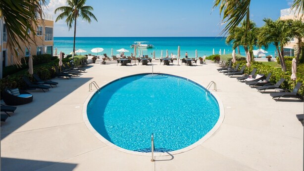 Ein Pool mit Liegestühlen und Sonnenschirmen, klares blaues Wasser und Blick auf den Ozean.