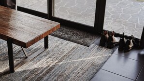 Um banco de madeira, um tapete estampado e um par de sapatos perto de uma porta de vidro.
