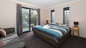 Quarto com uma cama grande, um sofá, uma mesinha de cabeceira com abajur e uma porta de vidro corrediça para um jardim.