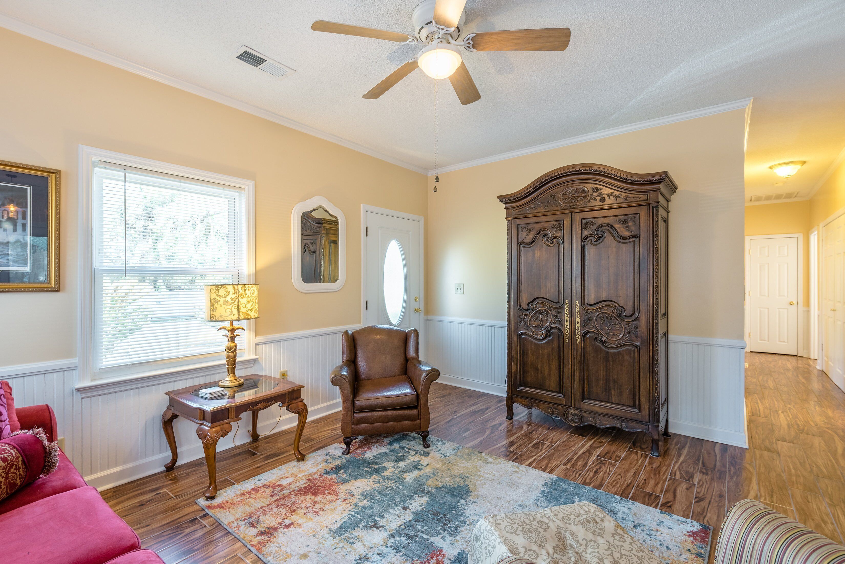 A room with a ceiling fan, a wooden cabinet, a red sofa, and a patterned rug.