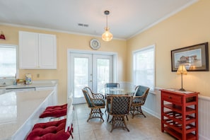 A kitchen with a dining table, chairs, a red side table, and a hanging light fixture.