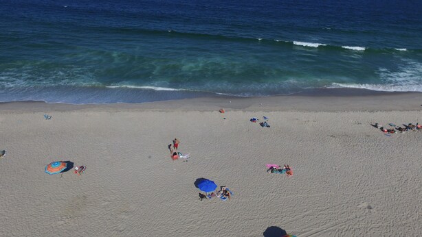 Ein Strand mit badenden Menschen und Sonnenschirmen, die Schatten spenden.