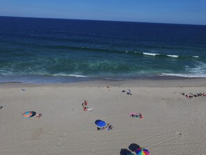 A beach with people sunbathing and swimming, and a few umbrellas providing shade.