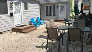 Eine Terrasse mit Gartenmöbeln, darunter Stühle und ein Tisch, sowie ein kleiner Trittstufenbereich, der zu einer Tür führt.