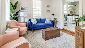 Ein Wohnzimmer mit einem blauen Sofa, zwei rosa Sesseln, einem Holztisch und einem gemusterten Teppich.