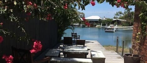 An outdoor patio with a pool, wooden furniture, and a view of a building across the water.