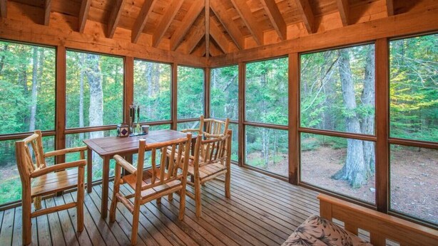 A wooden cabin with a dining table and chairs, large windows, and a ceiling light. - Unique Nature Inspired Home in Woods next to Lake (Mt Desert)