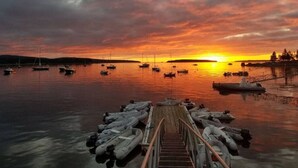 A wooden dock leading into calm water with several boats anchored. - Unique Nature Inspired Home in Woods next to Lake (Mt Desert)