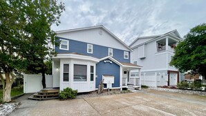 A two-story residential building with a bay window, a covered porch, and a small front yard with gravel and a tree. - Just Steps to the Beach! (Virginia Beach)