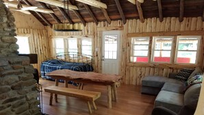 L’intérieur d’un chalet rustique est aménagé avec une table à manger en bois, des bancs, un canapé et un mur en pierre.