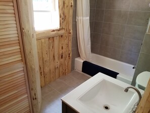 Une salle de bain avec un mur en bois, une baignoire, un lavabo blanc et une fenêtre.