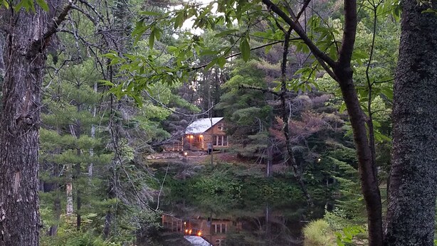 Une cabane avec un étang devant, entourée d’arbres.
