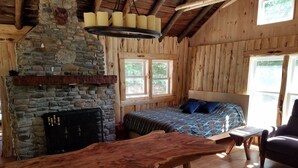 Une pièce rustique en bois, avec une cheminée en pierre, un lit recouvert d’une literie bleue et une table en bois.