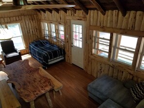 L’intérieur d’un chalet rustique, avec un lit, une chaise, un canapé et une table en bois.
