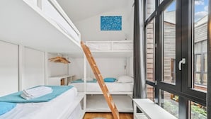 Habitación tipo dormitorio con literas, una escalera, un banco y un ventanal grande.