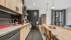 Cocina moderna con armarios de madera, un lavamanos de acero inoxidable y un comedor con mesa y sillas de madera.