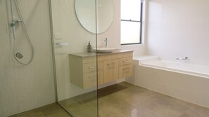Une salle de bain moderne avec une douche à parois de verre, un miroir rond, un lavabo avec un robinet et une baignoire.