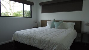 A bedroom with a large bed, two bedside tables, a window, and a view of trees. - Northern Haven Too, North Haven (North Haven)