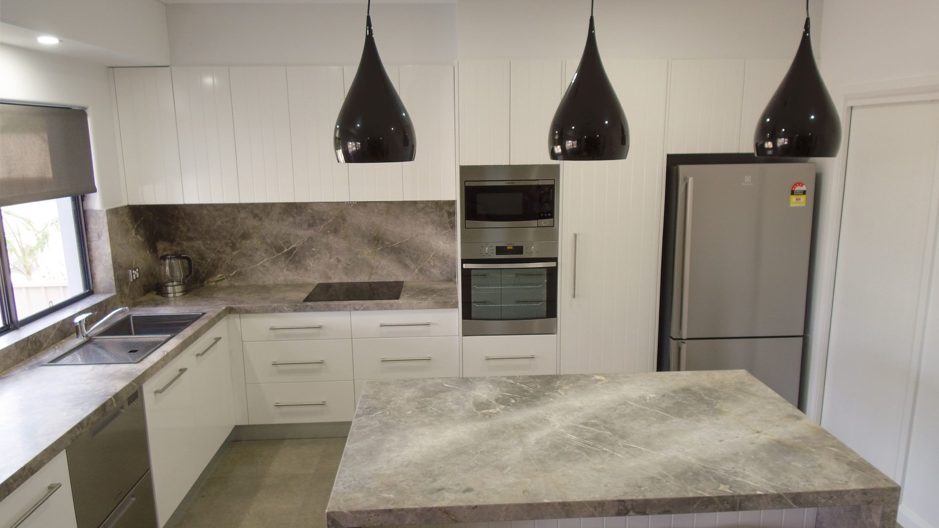 Eine moderne Küche mit weißen Schränken, einer Granit-Arbeitsplatte, einem Backofen, einer Mikrowelle, einem Kühlschrank und Pendelleuchten.