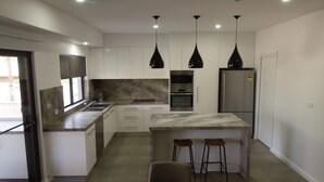 A modern kitchen with white cabinets, a marble countertop, a built-in oven, a refrigerator, and three pendant lights. - Northern Haven Too, North Haven (North Haven)