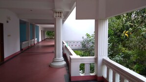 A corridor with white columns, red flooring, and a balcony with greenery.