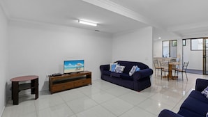 A modern living room with a dark blue sofa, a wooden TV stand, and a dining area with a table and chairs.