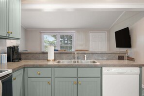 A kitchen with a double sink, a dishwasher, and a window with blinds.
