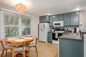 Een keuken met een eettafel, stoelen, een koelkast, magnetron, oven en een spoelbak.