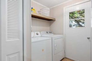 A laundry room with a washing machine, dryer, and a shelf with laundry supplies.