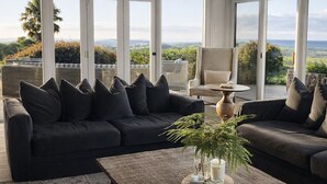 Een moderne woonkamer met een groot raam, een donkere bank, een bijzettafeltje en uitzicht op het groen.