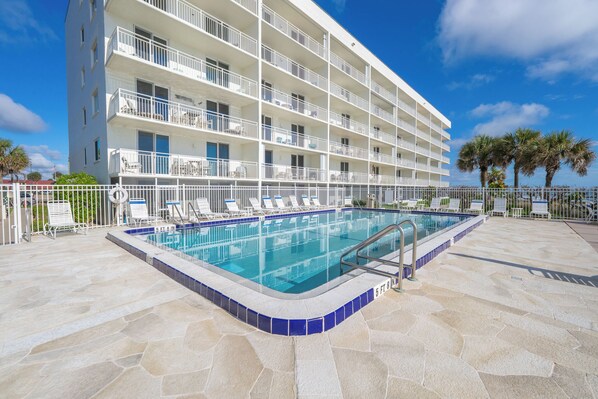 Un hôtel doté d’une piscine, de plusieurs balcons et offrant une vue sur un ciel d’un bleu éclatant.