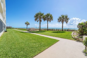 A well-maintained lawn, a concrete pathway, and a view of the ocean with palm trees. - Oceanfront Condo Steps to the Beach Heated Pool Sleeps 6 Unit 103 (Indian Harbour Beach)