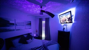 A bedroom with a bed, a ceiling fan, a TV on the wall, and a window with curtains.