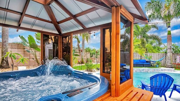 A hot tub area with a wooden deck, a pool, and outdoor seating.