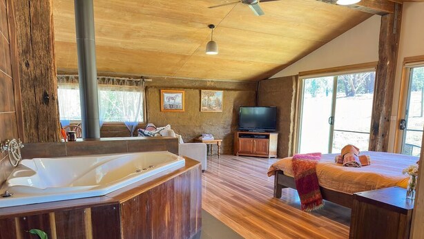 Ein geräumiges Zimmer mit einer großen Holzbalkendecke, einer Badewanne, einem Bett, einem Fernseher und einem Fenster mit Blick ins Freie.