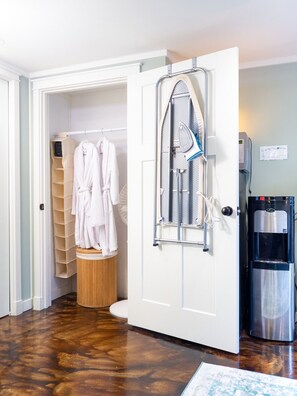 Een badkamer met een witte deur, een strijkplank, een handdoekhouder en een waterdispenser.