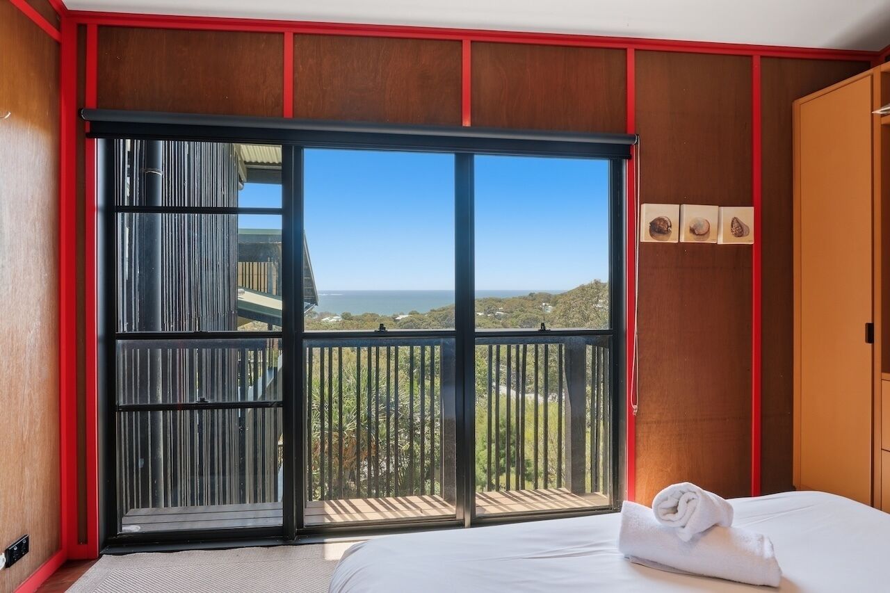 Une chambre d’hôtel dotée d’une grande porte-fenêtre coulissante donnant sur un balcon, d’un lit avec une serviette soigneusement pliée, et offrant une vue sur le paysage.