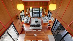 A spacious living area with a wooden floor, a central sofa set, a dining table with chairs, and large windows providing natural light.