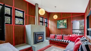 A cozy living room with a fireplace, a striped sofa, and a large window overlooking greenery.
