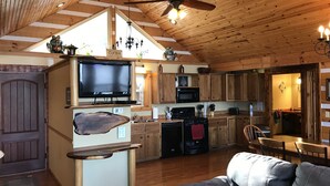 A cozy cabin interior with a wooden ceiling, a TV, a kitchenette, and a dining area. - ‘’Castle Colucci’’Magnet Indiana,a slice of Heaven where the world stands still. (Magnet)
