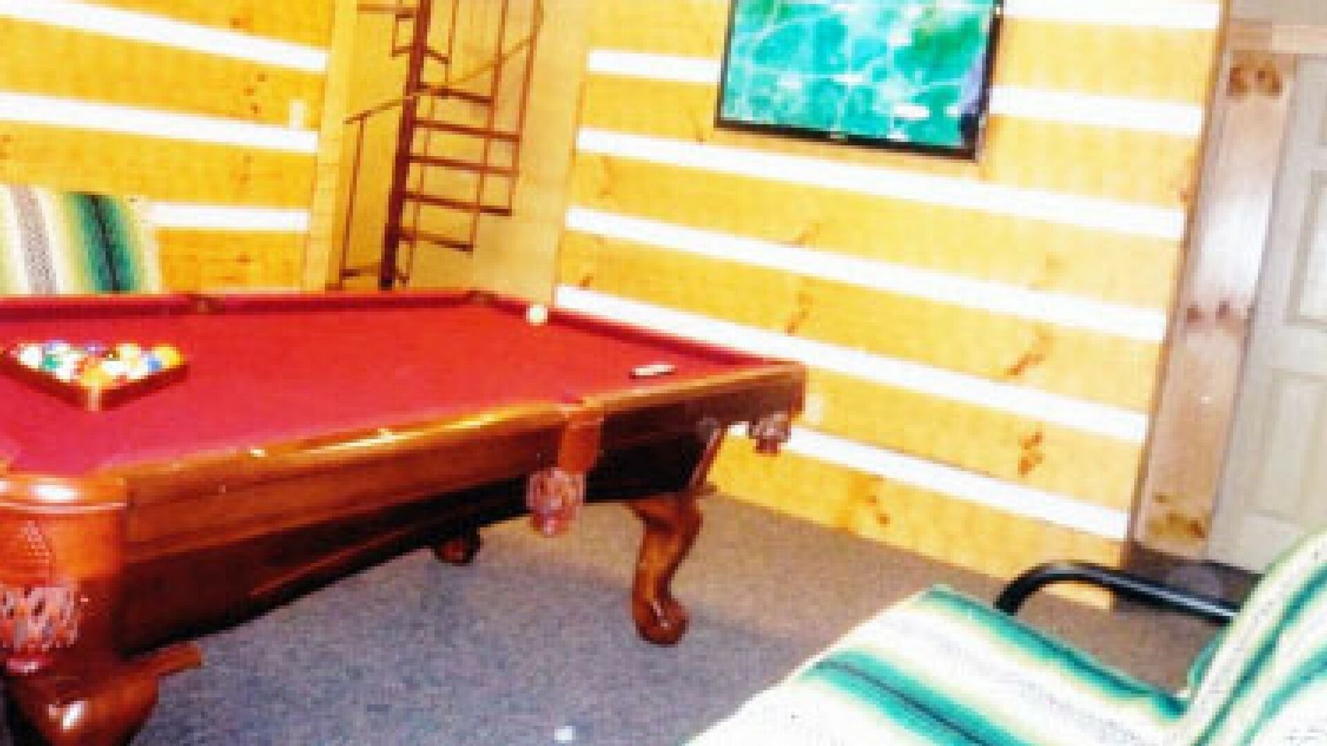 Una mesa de billar en una sala con paredes de madera y una escalera.